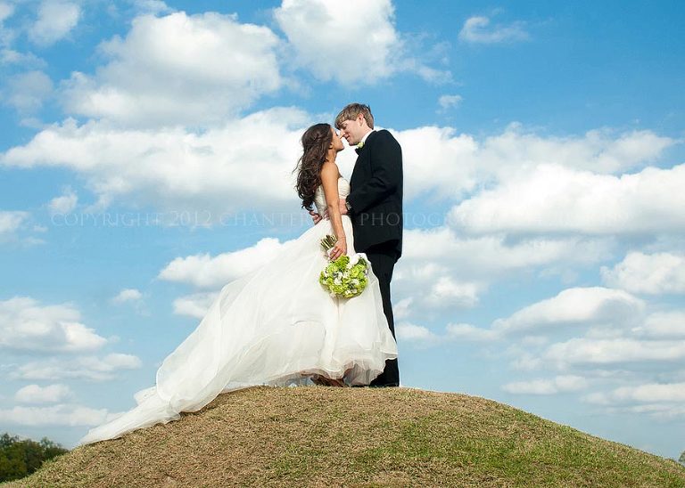 a bride and groom on a hill against a blue sky and white clouds in montgomery alabama