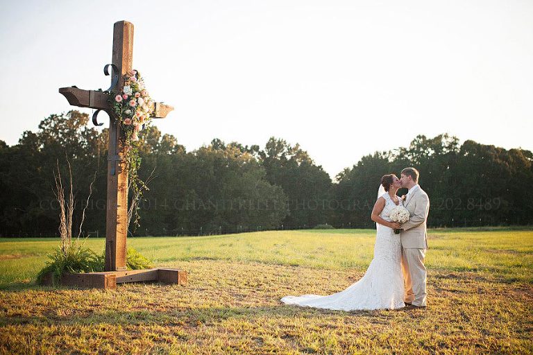 bride and groom with rustic cross in a field
