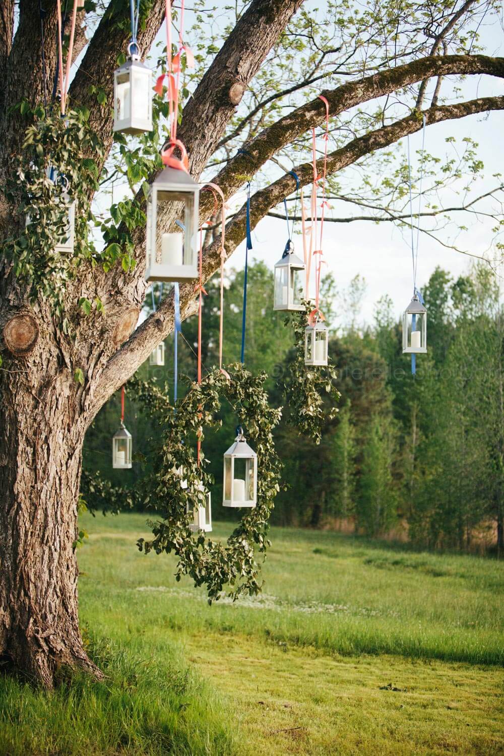 lanterns with candles hanging from trees with ribbon for wedding