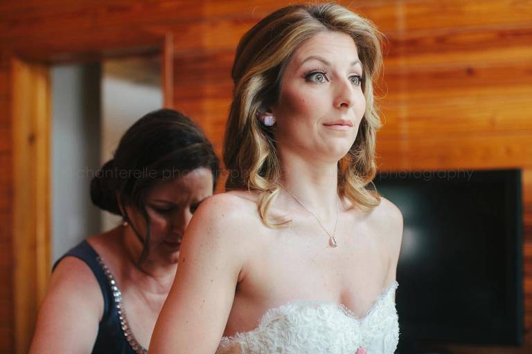 bride making funny face as mom zips up her dress