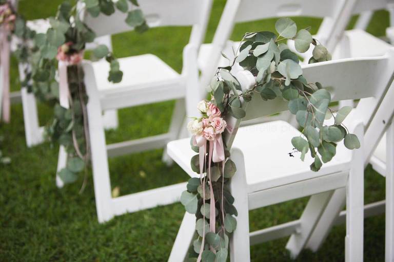flowers and greenery lining rows of chairs at wedding