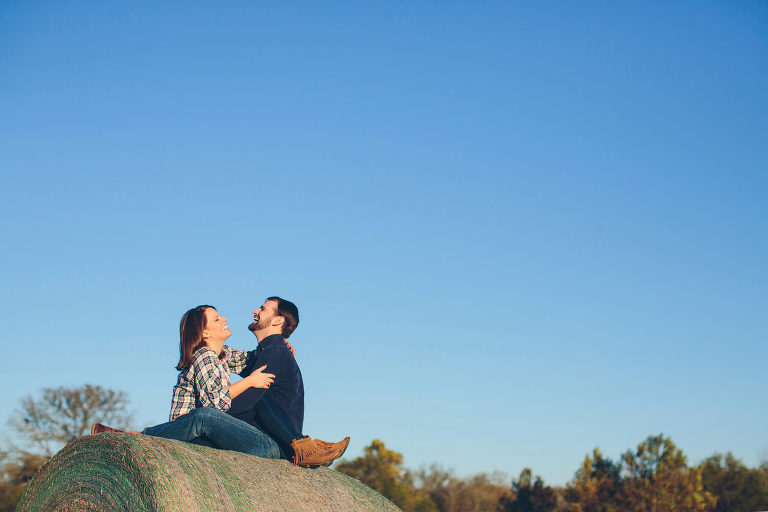 couple laughing on top of haybale in alabama farm engagement pictures