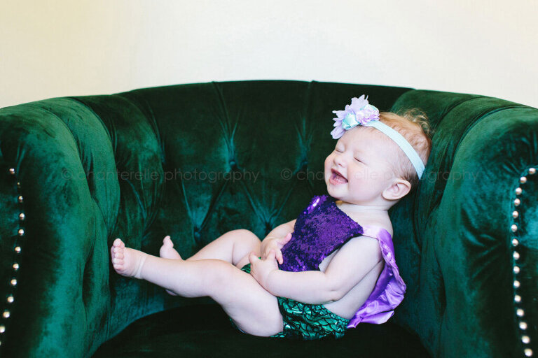 baby girl laughing in emerald green velvet chair